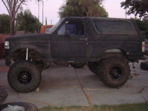 Lifted black Ford Bronco with large off-road tires, parked on a concrete driveway