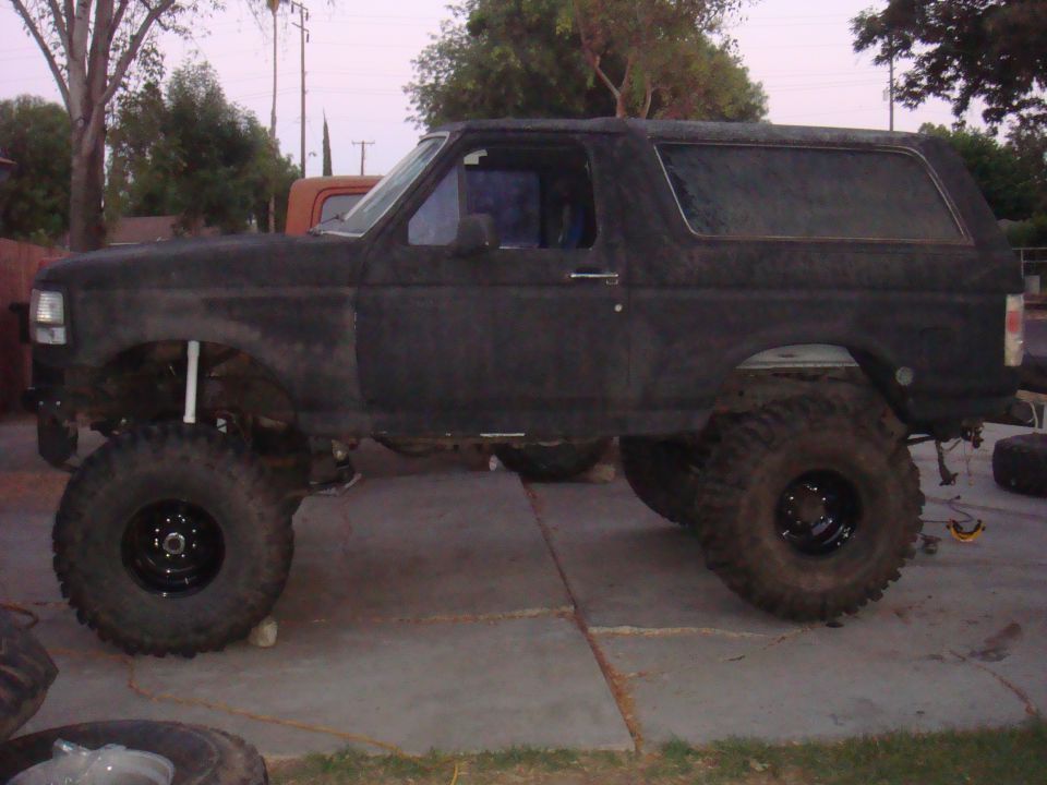 Lifted black Ford Bronco with large off-road tires, parked on a concrete driveway