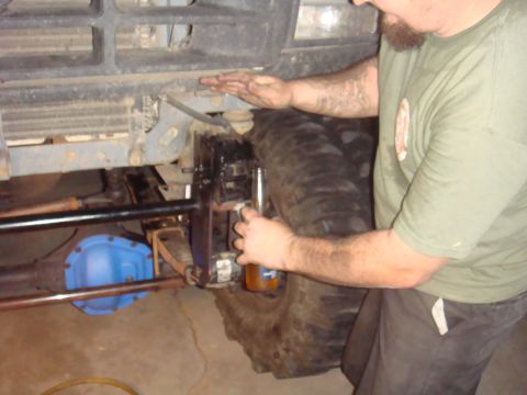 1992 Ford Bronco front axle and suspension with a person's hands working on the brake caliper