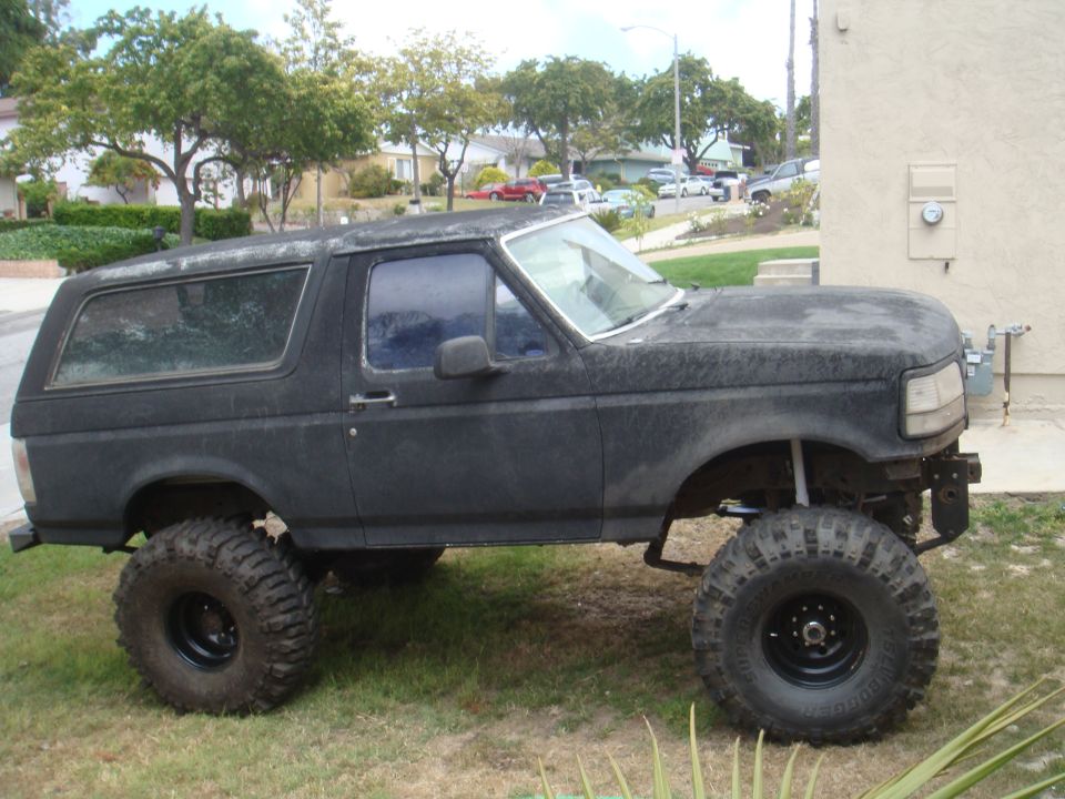 Lifted black Ford Bronco with large tires, parked on grass. Front bumper is removed