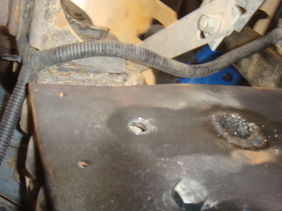 Close-up of rusty metal plate with a hole, wires, and suspension parts