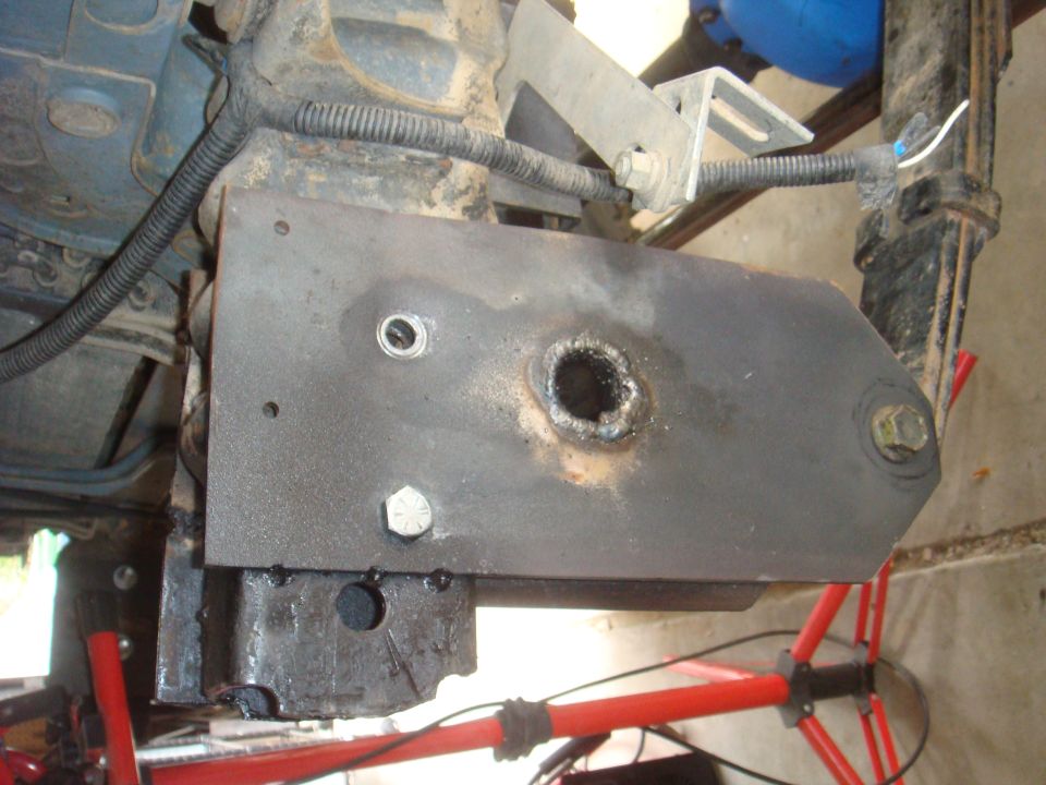 Close-up of a metal bracket bolted to a vehicle's frame, showing a hole with rough edges