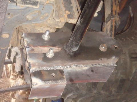 Close-up of a welded metal bracket attached to a vehicle's undercarriage with bolts