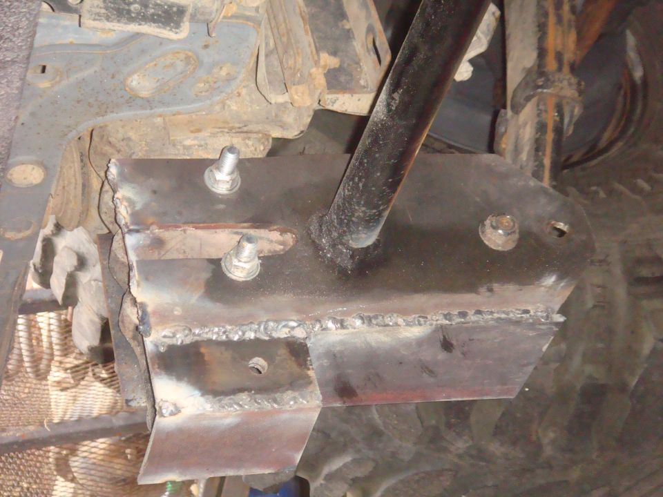 Close-up of a welded metal bracket attached to a vehicle's undercarriage with bolts