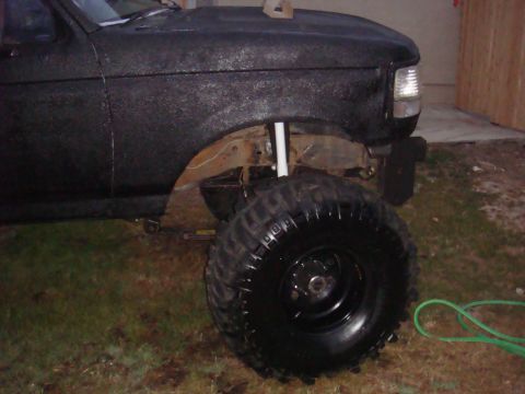 Black Ford F-Series truck with large off-road tires and lifted suspension. Front fender and wheel are visible