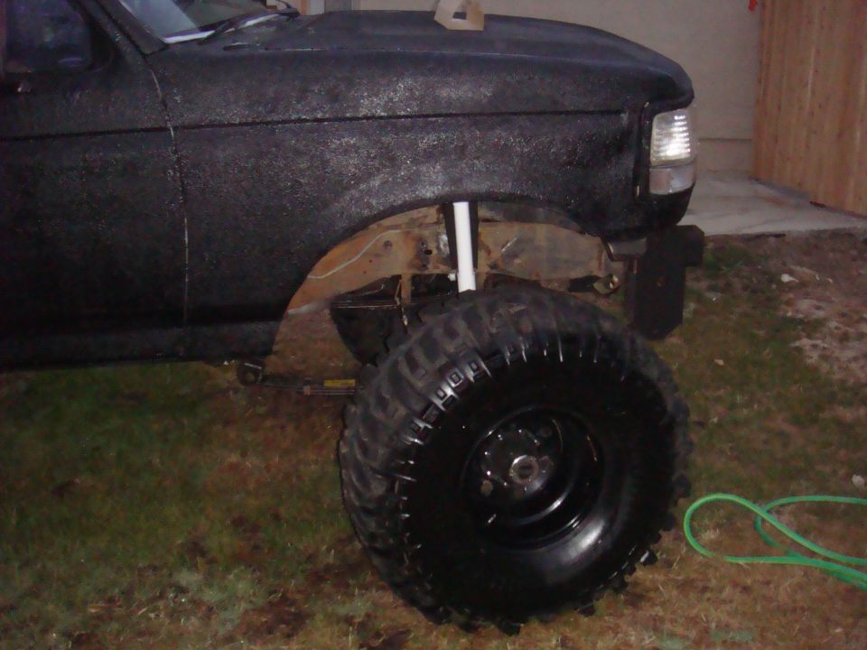 Black Ford F-Series truck with large off-road tires and lifted suspension. Front fender and wheel are visible