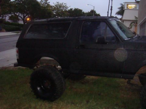 Black 1992 Ford Bronco parked on grass, side view, lifted suspension, dark tinted windows