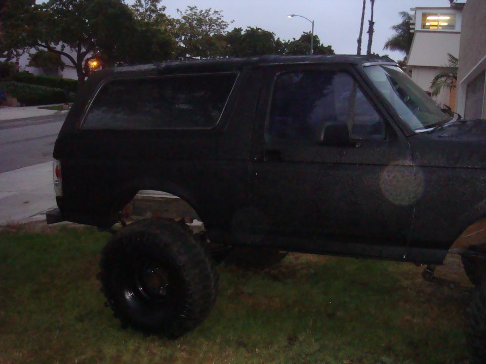 Black 1992 Ford Bronco parked on grass, side view, lifted suspension, dark tinted windows