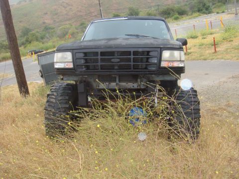 1992 Ford Bronco front view, lifted with large tires, parked in dry grass