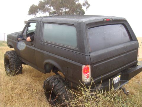 Black 1992 Ford Bronco with lifted suspension and oversized tires parked in dry grass