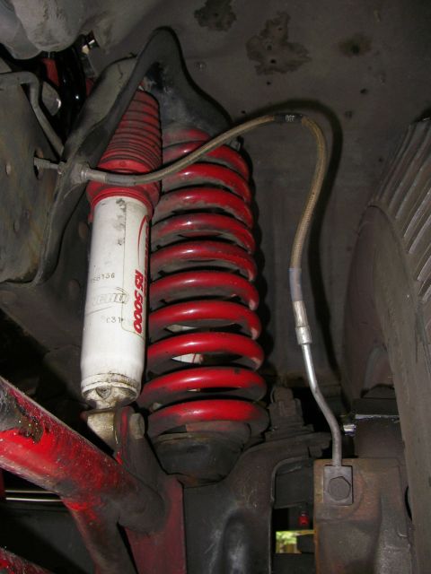 1990 Ford Bronco - Close-up of a vehicle's suspension system, showing a red coil spring and a white shock absorber.