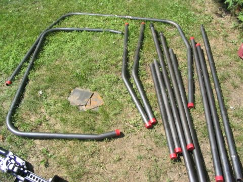 1986 Ford Bronco - Metal tubing for a roll cage is spread out on a grassy area, ready for assembly.