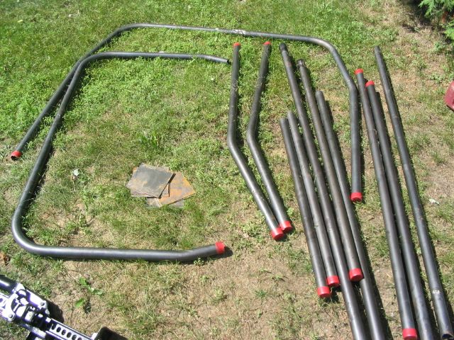 Steel roll cage tubing with red end caps laid out on grass