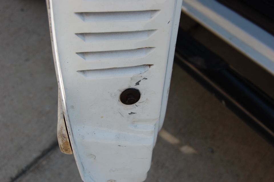 White vehicle fender with horizontal vents and a bolt hole. A black bar is visible to the right