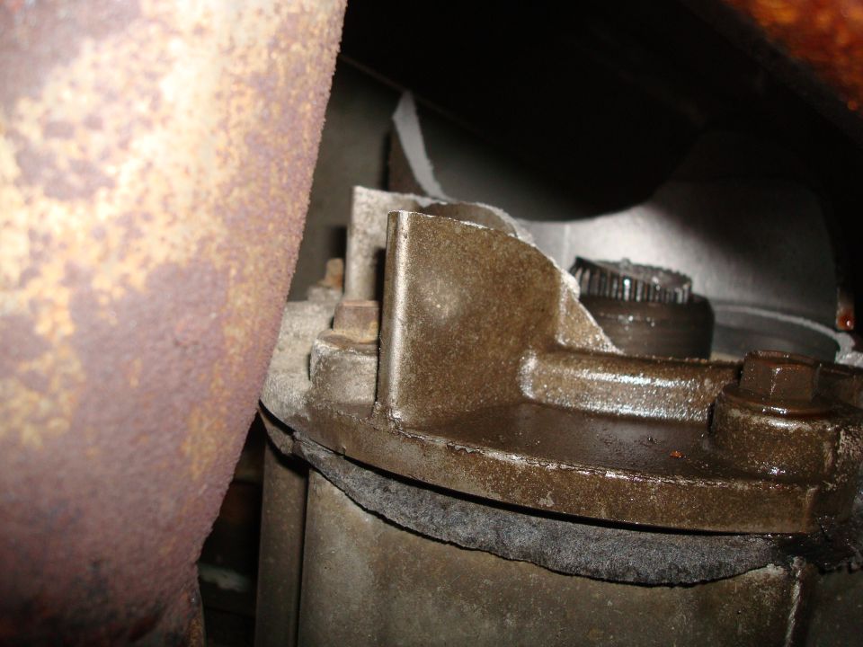 Close-up of vehicle's transmission part with rusty exhaust pipe. Supermotors.net logo visible