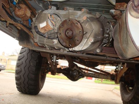 1996 Ford Bronco - Underside view of a vehicle's transfer case and drivetrain, showing rusty parts and a large tire.