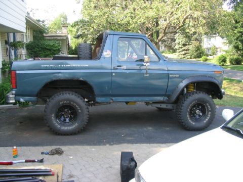 1986 Ford Bronco - This lifted blue 1986 Ford Bronco features off-road tires and a website decal on its side.