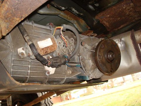 1996 Ford Bronco - Underside view of a vehicle's transfer case and driveshaft, exhibiting signs of rust and age.