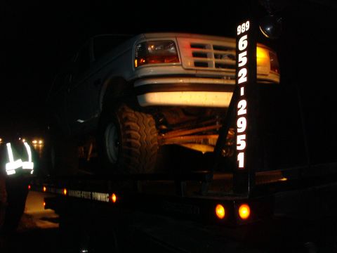 1996 Ford Bronco - A white Ford F-Series truck is being towed at night, with a tow company's phone number visible on the back of the tow truck.