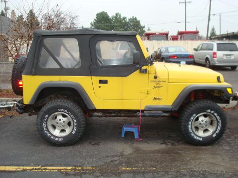 1996 Ford Bronco - A yellow Jeep Wrangler is seen from the side, a black soft top and a spare tire mounted on the rear.