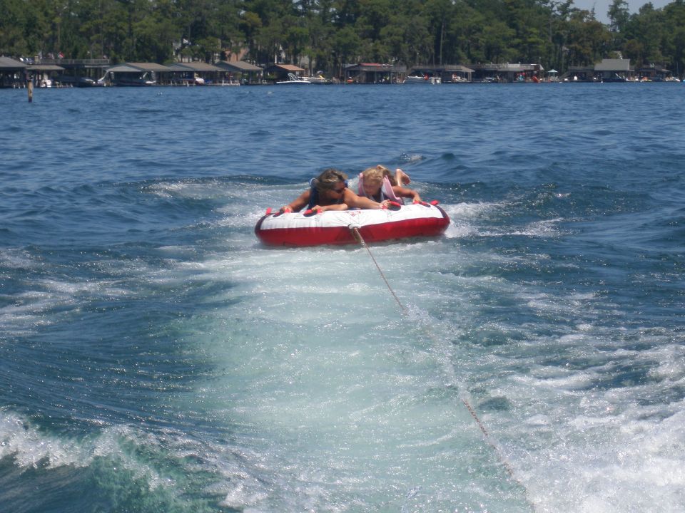 Two kids on a red and white inflatable tube being pulled across a lake