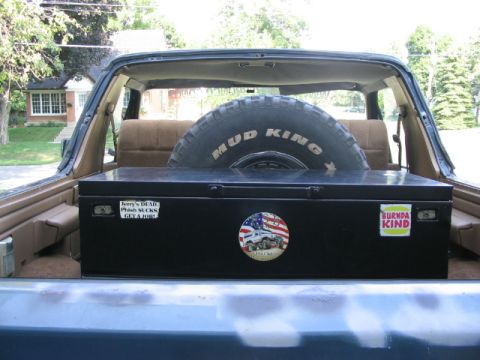 1986 Ford Bronco - Spare tire and toolbox stored in the cargo area of a vehicle.