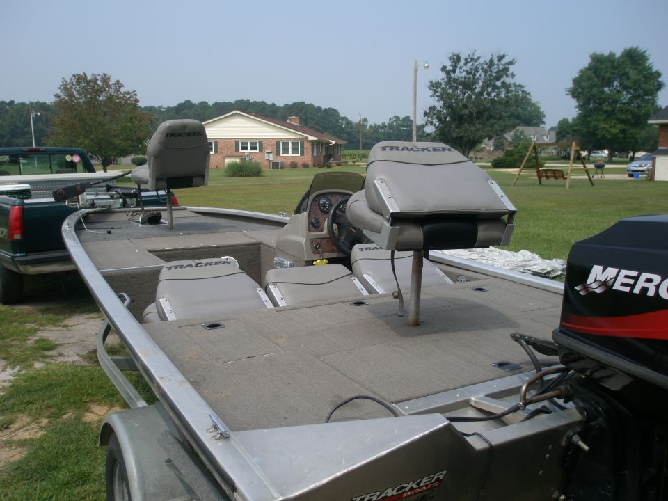 Tan Tracker aluminum bass boat on trailer with Mercury outboard, green pickup towing in background