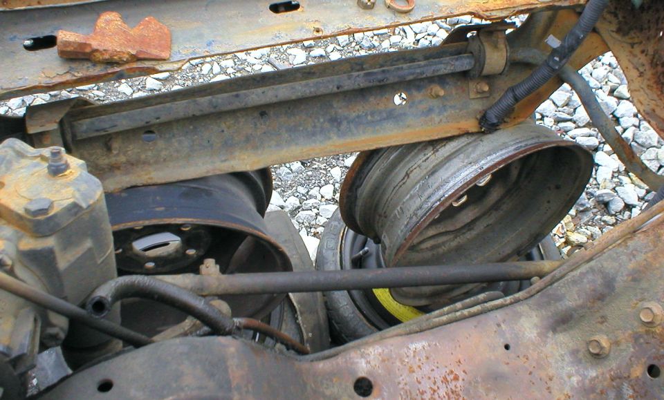 Rusty leaf-spring rear suspension and brake drums viewed from beneath a vehicle on gravel