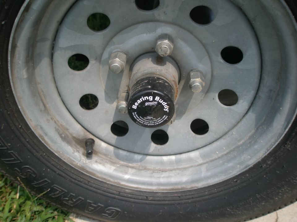 Trailer wheel with a black Bearing Buddy hub cap, gray metal rim, and tire