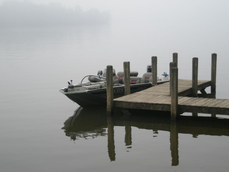 Bass boat docked on a foggy lake, with wooden posts and reflections
