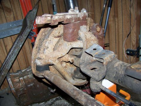 1992 Jeep YJ - Close-up view of a heavily rusted front axle assembly, likely from an older vehicle, with a large metal tool positioned nearby.