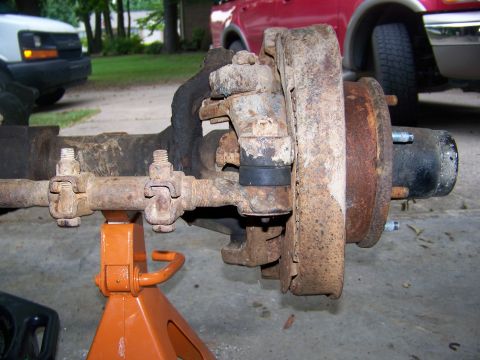 1992 Jeep YJ - This heavily rusted front axle assembly is supported by an orange jack stand, with other vehicles visible in the background.