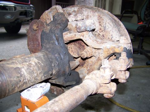 1992 Jeep YJ - Close-up of a heavily rusted axle assembly, with a red truck visible in the background.