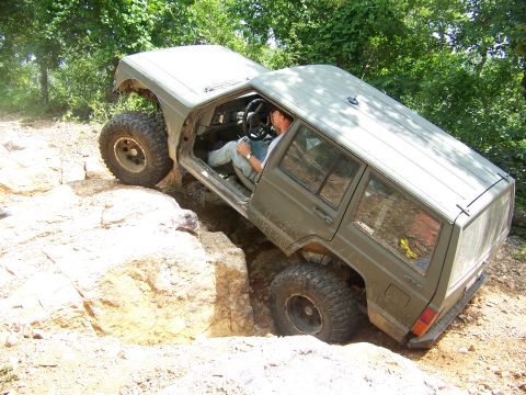 1992 Jeep YJ - This Jeep Cherokee XJ is shown attempting a challenging off-road course with large rocks and uneven terrain.