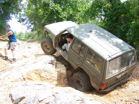 1992 Jeep YJ - A Jeep Cherokee XJ is shown off-roading on a rocky trail, with one wheel significantly elevated.