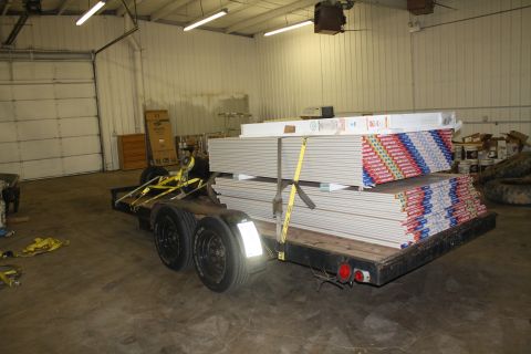 1985 Ford F-350 - A trailer carrying drywall is parked inside a warehouse with a large garage door in the background.