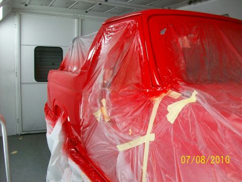 1985 Ford Bronco - A red truck cab is being prepped for painting inside a booth.