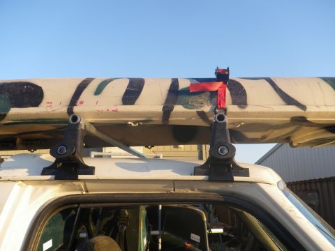 1991 Ford Bronco - A camouflage canoe is secured to the roof rack of a white vehicle under a clear blue sky.