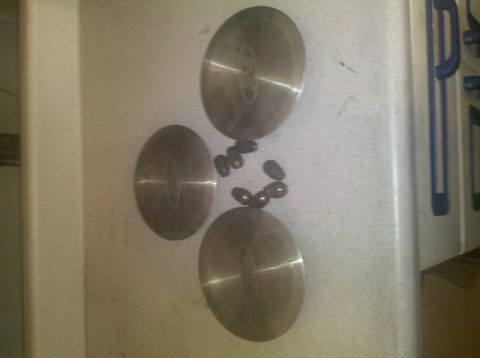 1992 Ford Taurus - Three Ford hubcaps and lug nuts are laid out on a counter surface.