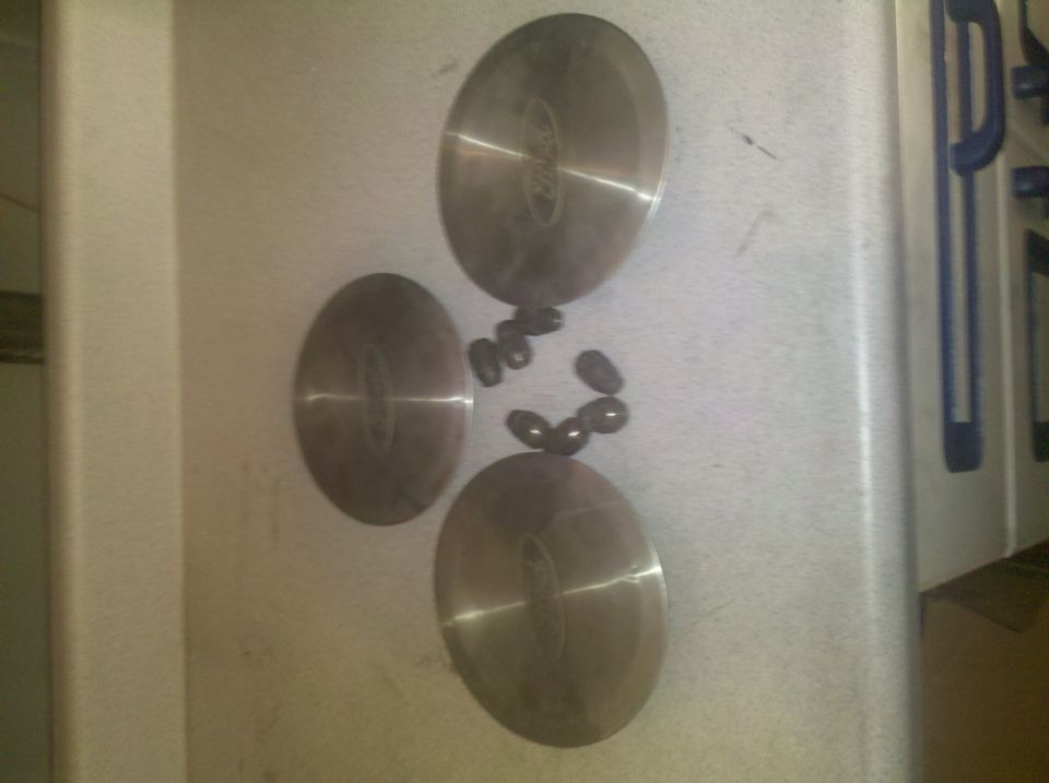 Three Ford hubcaps and lug nuts on a counter