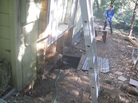 1989 Ford Bronco - A person stands in a wooded area near a ladder and a building with exposed foundation, suggesting ongoing construction or repair work.