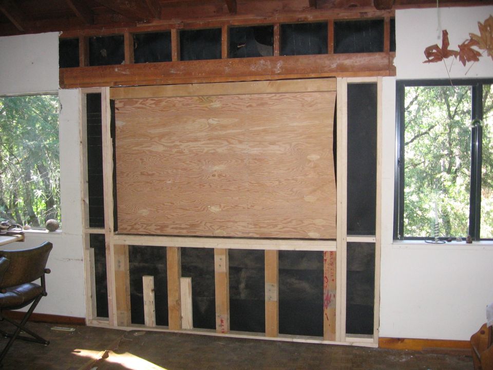 Interior of a room under construction with plywood covering a large opening and exposed wooden studs