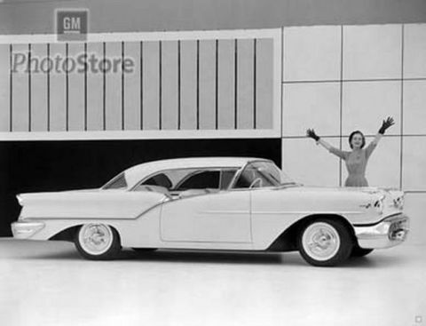 1991 Ford Crown Victoria - A 1955 coupe is displayed with a woman posing behind it, with a GM PhotoStore sign in the background.