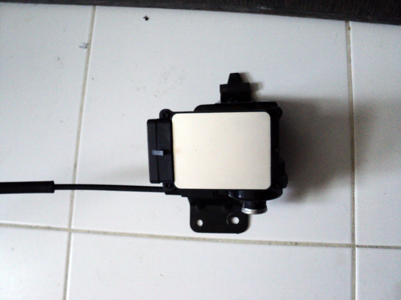 Black cruise control module with a white label and a cable attached, resting on a tiled surface