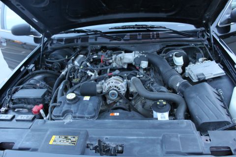 2007 Ford Crown Victoria - Engine bay of a black Ford sedan photographed with the hood up, showing a modular V8 with cast intake manifold, alternator, black plastic a…