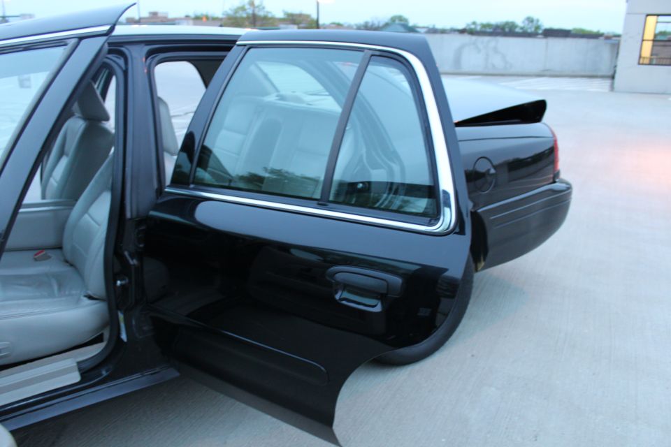Black sedan with doors open, showing light grey interior. Rear quarter panel and trunk are visible
