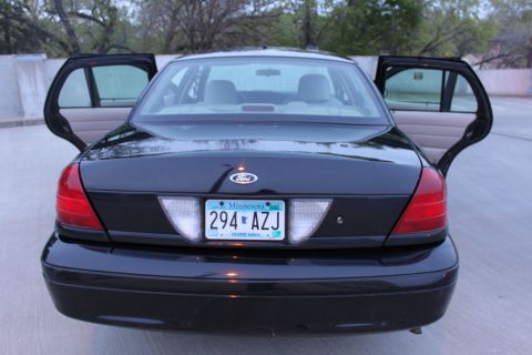 2007 Ford Crown Victoria - Straight-on rear view of a black Ford Crown Victoria with both left and right doors open, showing the gray interior and headrests through t…