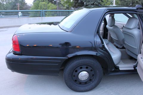 2007 Ford Crown Victoria - Low three-quarter rear view of a black full-size sedan with the rear door open, showing gray cloth/vinyl rear bench and front bucket seats.…