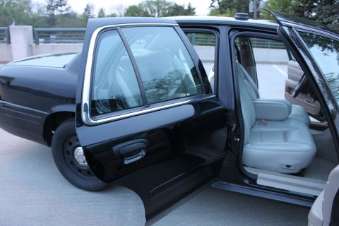 2007 Ford Crown Victoria - Both passenger-side doors of a black full-size sedan stand open, showing the gray front bucket seat, rear bench and bare rubber-matted door…