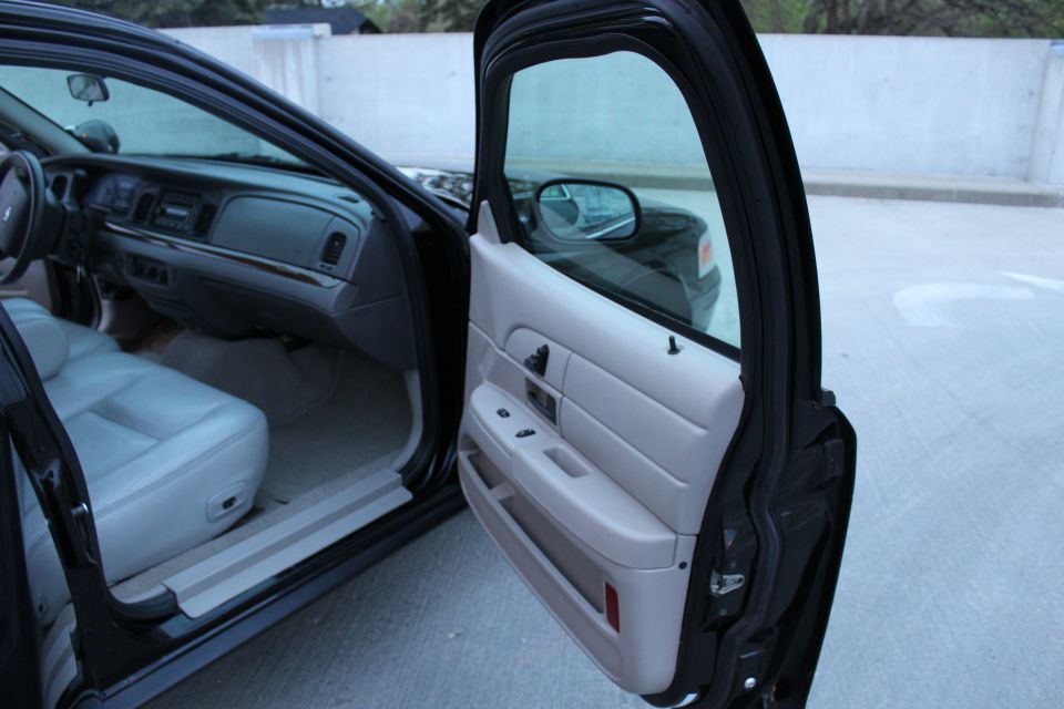 Open passenger door of a black sedan showing gray door panel, leather seat and wood-trim dash